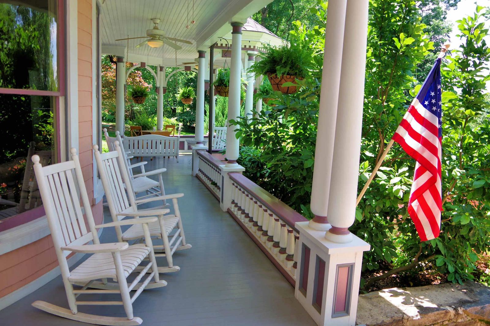 Wraparound porch with white rocking chairs and hanging ferns