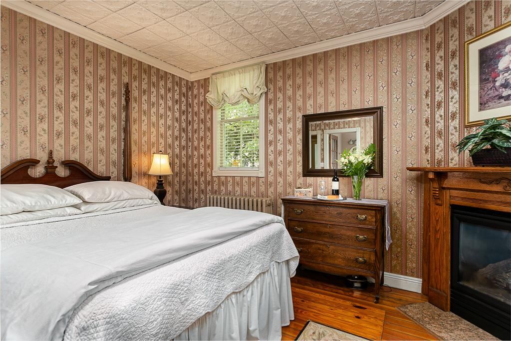 Main house guest room with striped wallpaper, antique dresser and fireplace