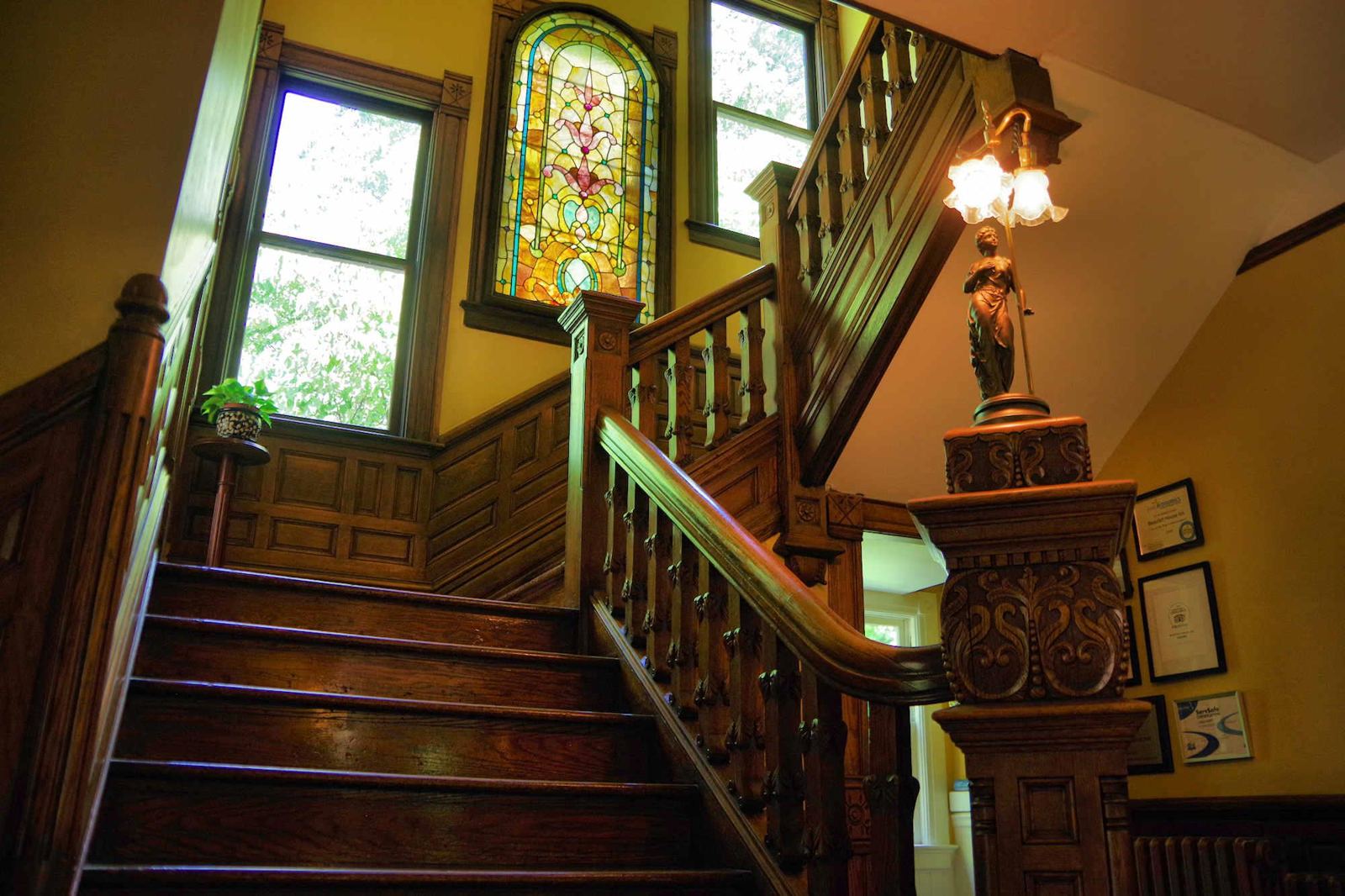 Grand wooden staircase with stained glass window and carved newel post lamp